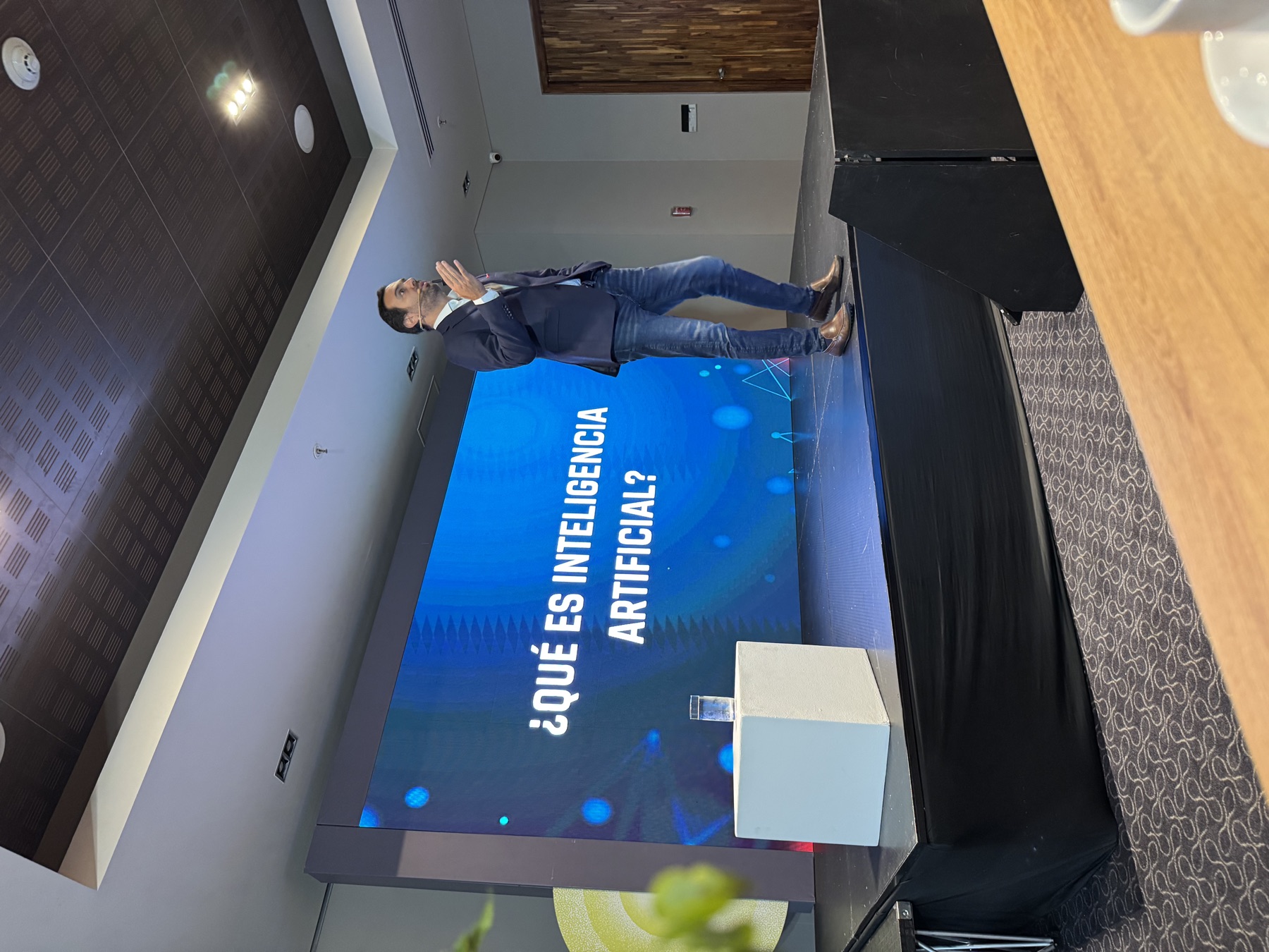 Conferencista sobre un escenario frente a una pantalla con la pregunta qué es inteligencia artificial